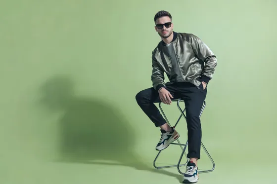Man In A Metallic Jacket And Black Pants Sitting On A Stool