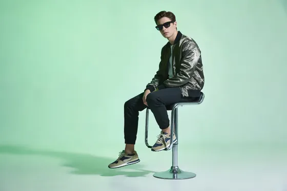 Man Sitting On A Stool In Front Of A Green Background